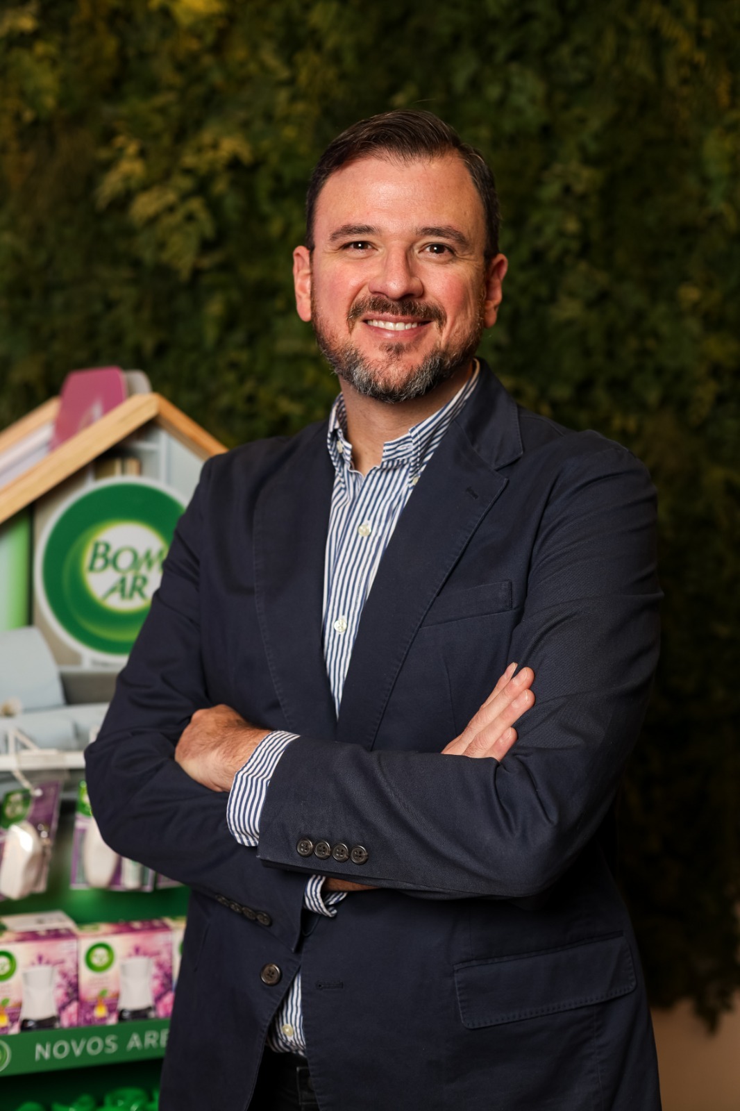 Imagem de um homem de braços cruzados com uma prateleira de produtos atrás dele